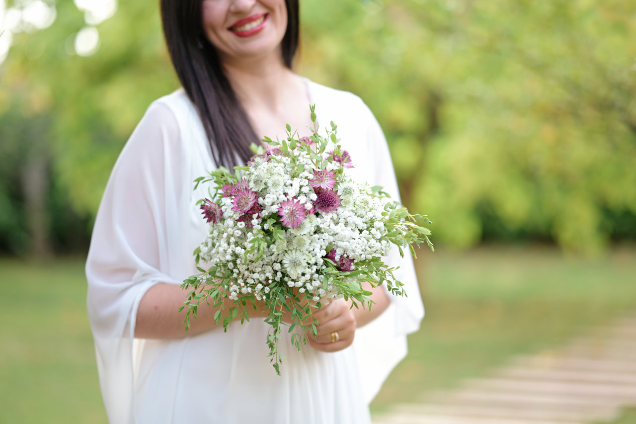Portret mladenke koja se smije, s vidljivim usnama u blagom osmijehu i buketom u rukama – trenutak tihe radosti.