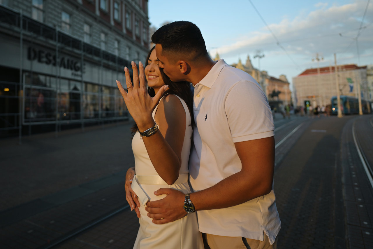 Mladić nježno ljubi djevojku u obraz u zagrbeačkoj Ilici. Djevojka na ruci ponosno pokazuje zaručnički prsten.