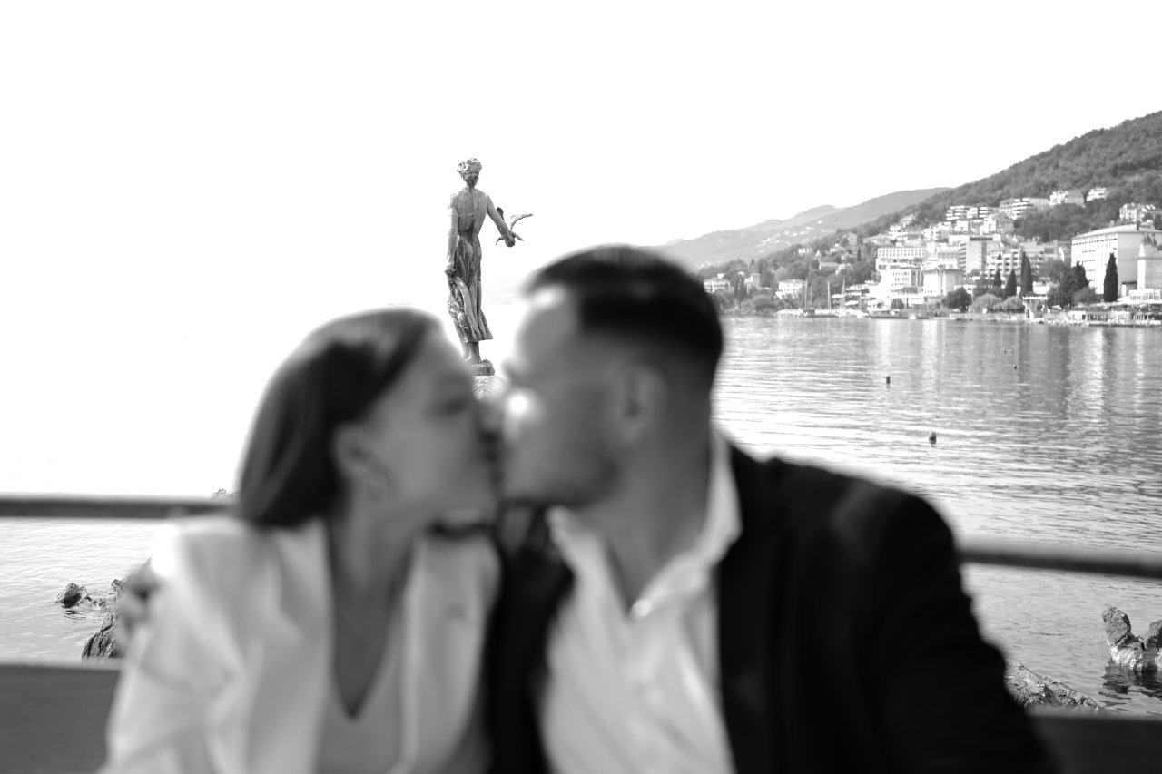 Upravo zaručen mladi par se ljubi ispred čuvene Djevojke s galebom na opatijskoj rivi, fotografija prosidbe u Opatiji.