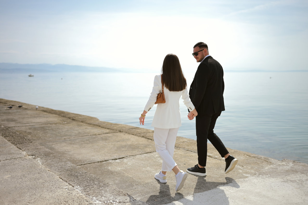 Mladi, zaljubljeni zaručeni par u elegantnoj odjeći drži se za ruke i zaljubljeno se gleda u oči na rivi u Opatiji, nakon zaruka.