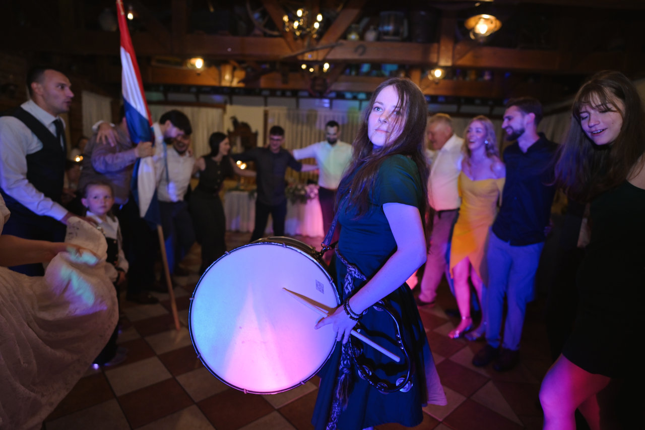 Proslava vjenčanja; mlada bubnjarica na plesnom podiju s bubnjem oko vrata, okružena rasplesanim ljudima.