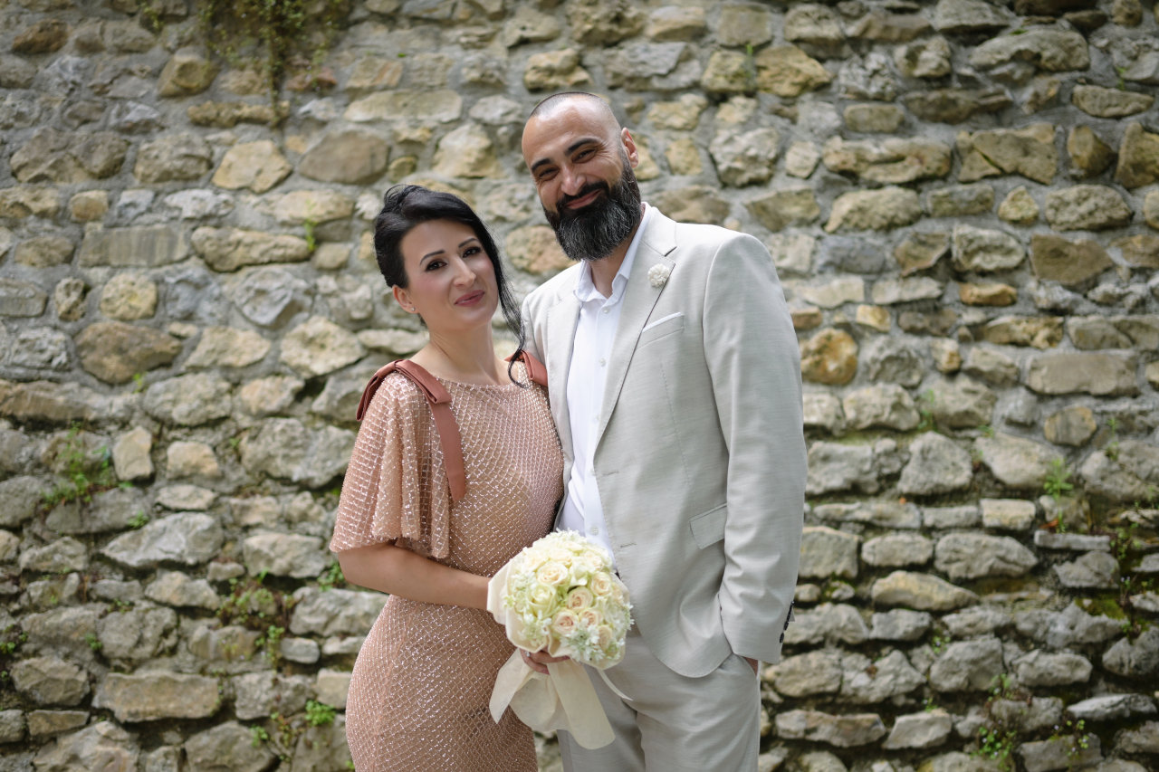 asmijani mladenci s buketom poziraju ispred kamenog zida na Strossmayerovom šetalištu u Zagrebu tijekom vjenčanja.