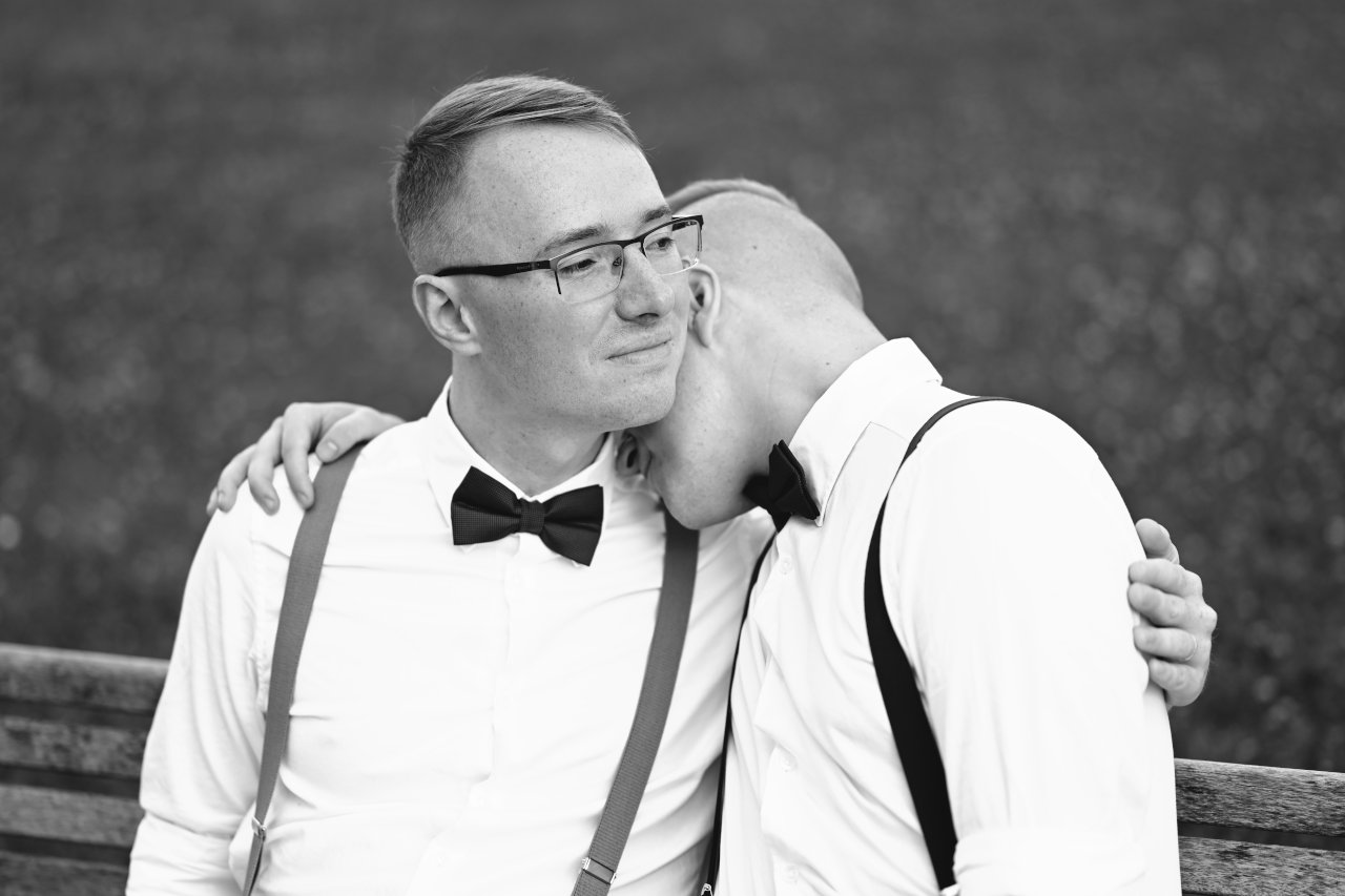 Crnobijeli portret istospolnog para na klupi u parku tijekom fotografiranja vjenčanja.