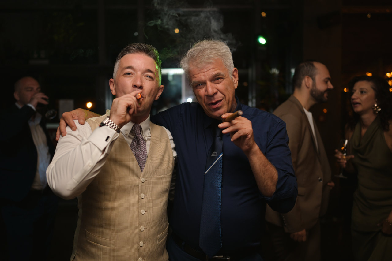 Mladoženja i voditelj ceremonije na proslavi vjenčanja; oboje sa zapaljenim kubanskim cigarama.