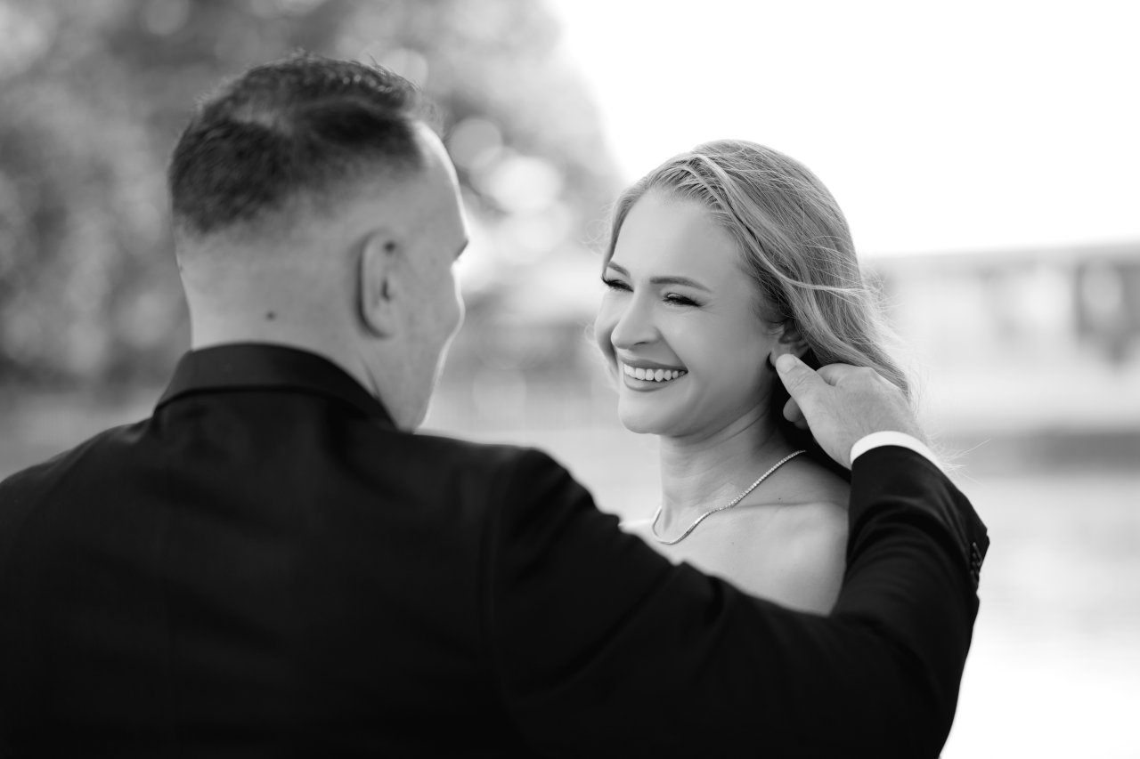 Emotivan crnobijeli portret mladoženje koji popravlja kosu nasmijanoj mladoj na dan vjenčanja.